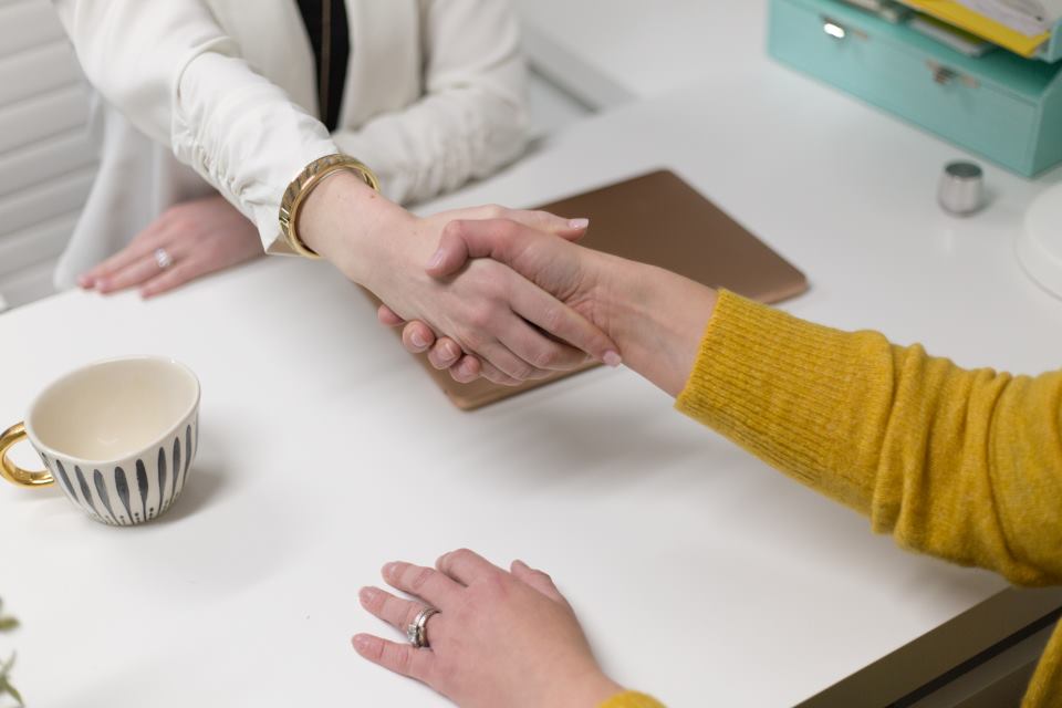 Two people shaking hands over a desk at the close of a meeting
