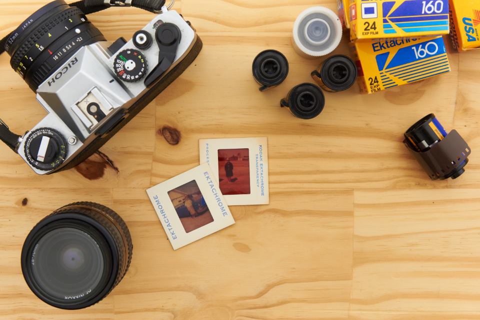 A film camera, lenses and slide frames laid out on a wooden table