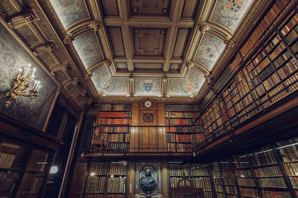 A classical library hall with tall wooden bookshelves and a decorated ceiling