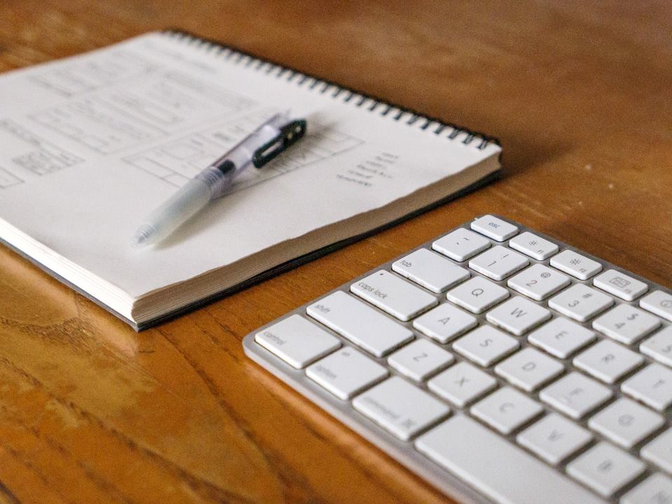 Notebook with handwritten notes and a keyboard on a warm wooden desk